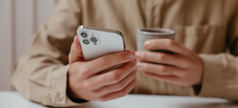 čovek drži mobilni telefon i šoljicu