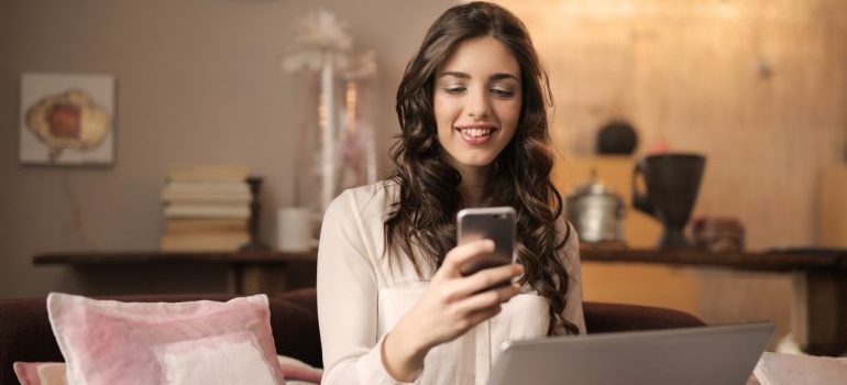 Girl with laptop holding her phone and looking at it.