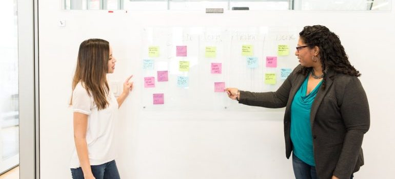 Two women in front of a whiteboard, discussing dealing with negative customer reviews.