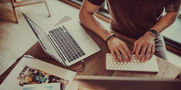 Person typing on a remote keyboard next to a laptop.