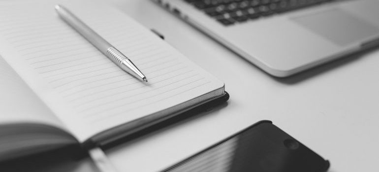 a notebook with a pen, next to a cell phone