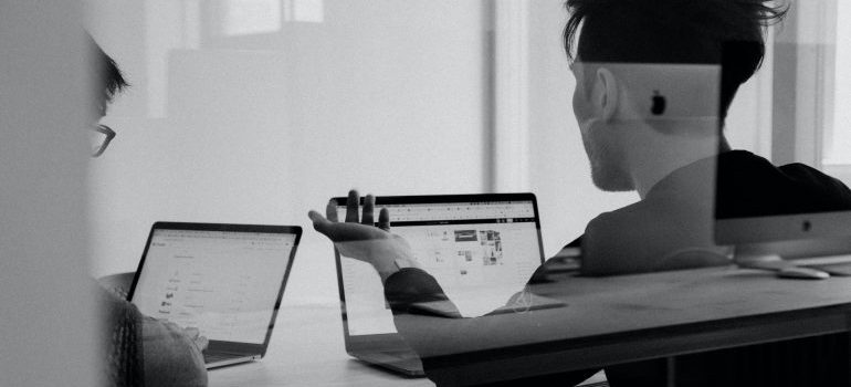 two people in front of laptop computers in black and white