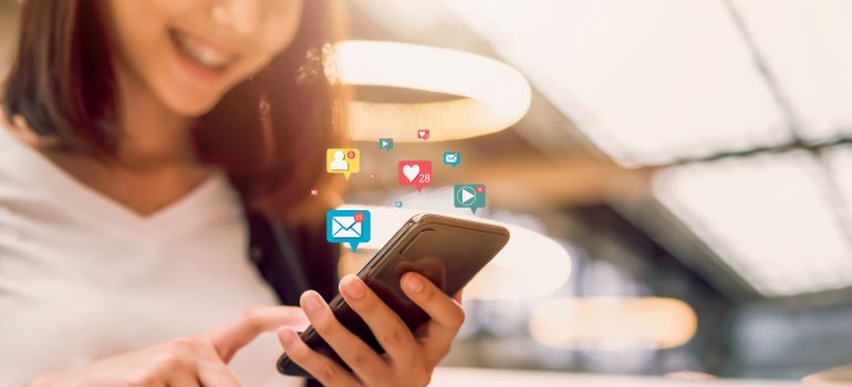 Girl looking at her phone, with social media icons in the air.
