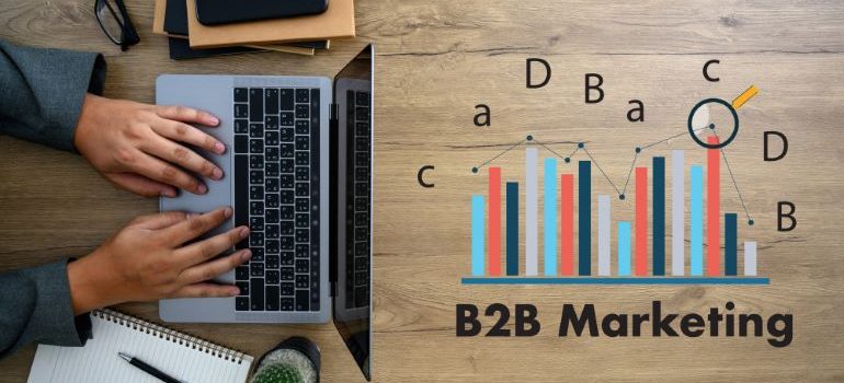 B2B marketing under a stats illustration, next to a laptop on a wooden table.
