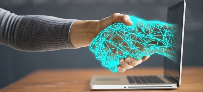 A man shaking a digital hand coming out of a laptop screen.
