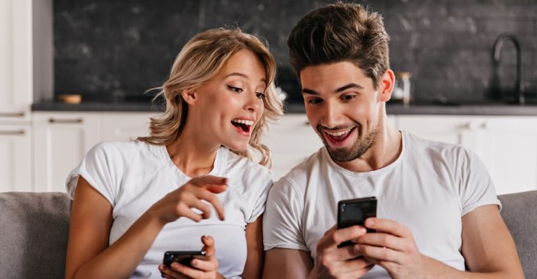 A couple looking at their mobile phones with awe