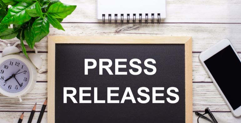Press Releases on blackboard, with notepad, phone, and clock on desk.