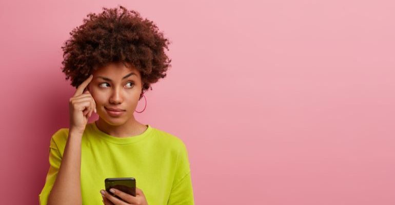 Woman with phone in her hand, with index finger on her forehead.