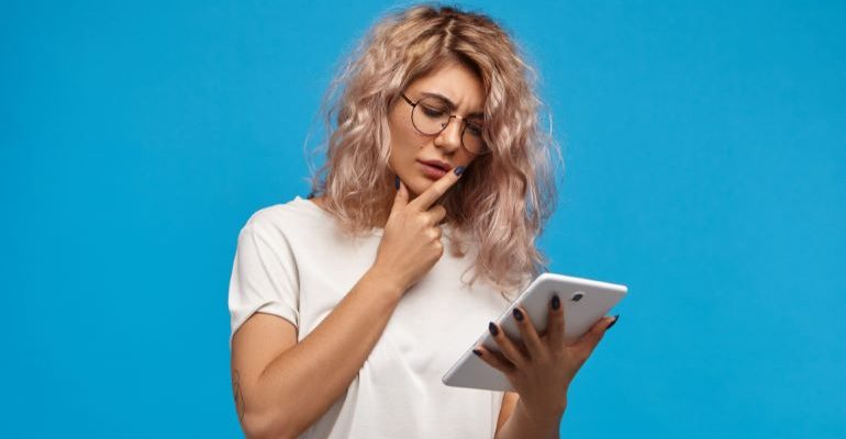 Woman touching her chin and looking at a tablet.