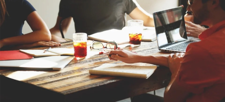 People around a table having beers over books.