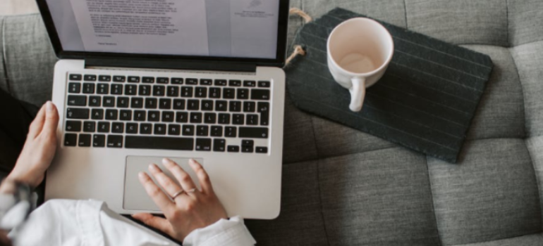 A close-up of a woman using a laptop on a grey couch.
