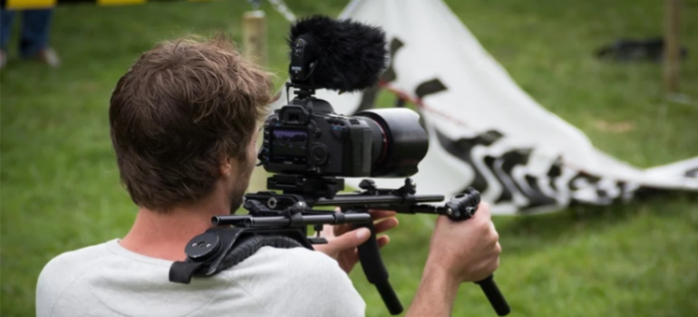A male reporter in a white shirt holding a camera.