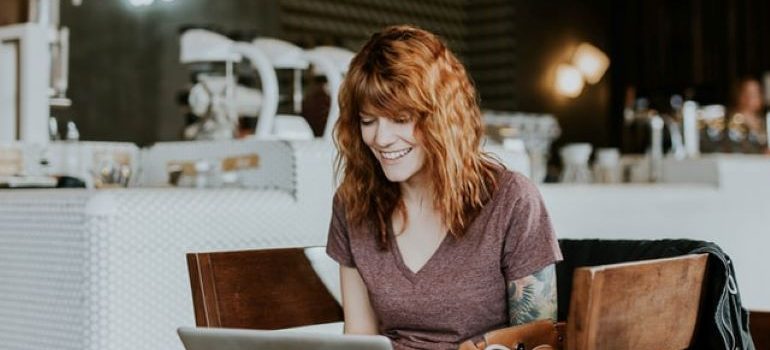 Woman with a tattoo on her left arm sitting at a table and using her laptop