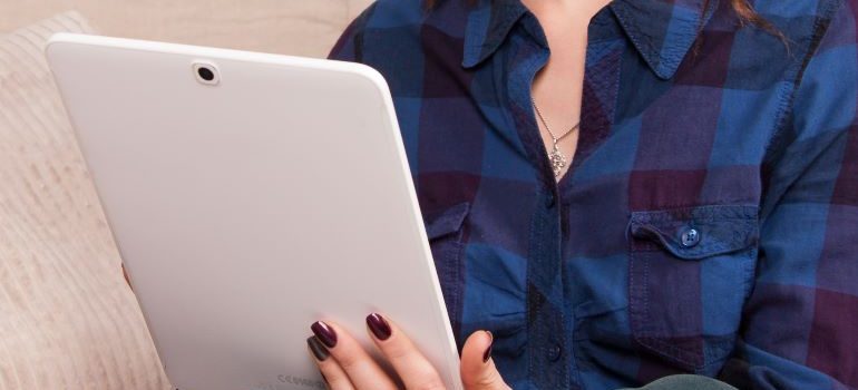 Woman wearing a black and blue shirt sitting and reading something on a large white tablet
