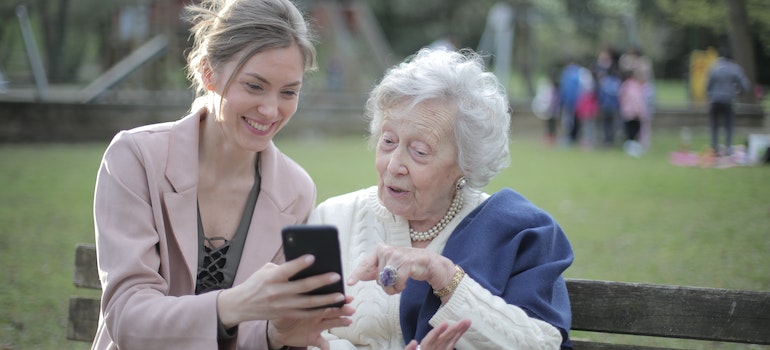 Grandmother and her granddaughter sitting on a bench and looking at a smartphone