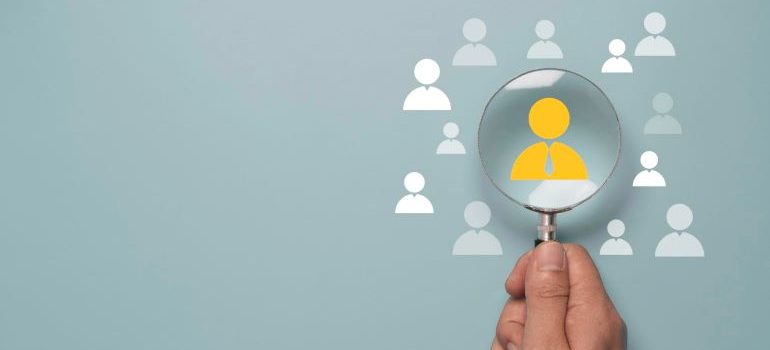 Hand holding a magnifying glass over audience icons.