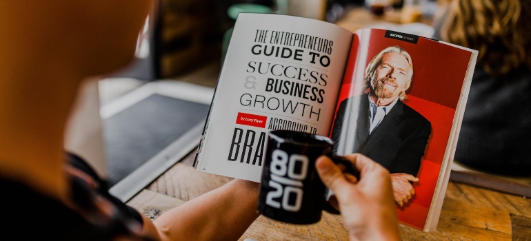 Person holding a black coffee mug and reading a book about personal branding