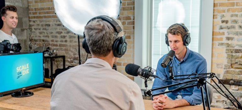 Two people talking on a podcast while sitting across each other at a desk