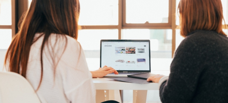 Two women sitting at a desk and looking at images on a laptop