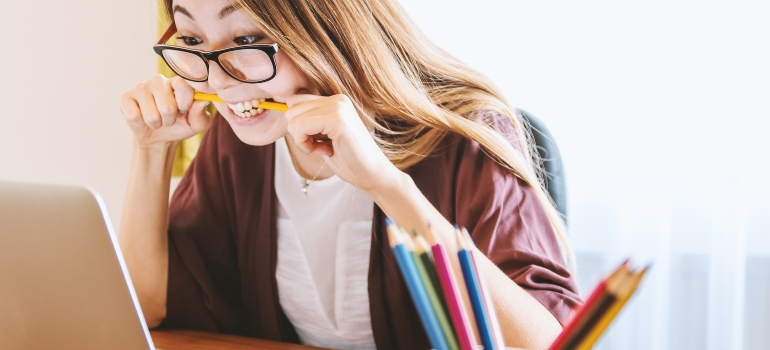 Young woman biting a pencil and looking at a laptop