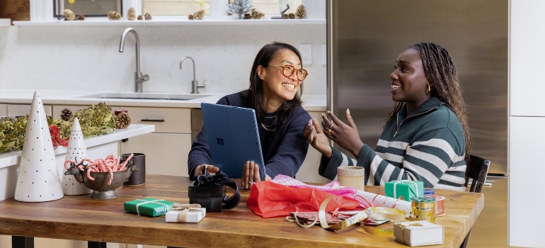 Two women sitting at a table in a kitchen and smiling