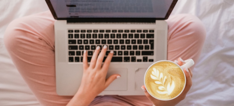 Person with a laptop in their lap holding a cup of coffee in their right hand
