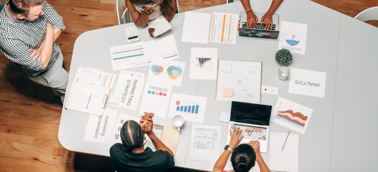 Five people sitting around a gray table covered with papers and having a meeting 