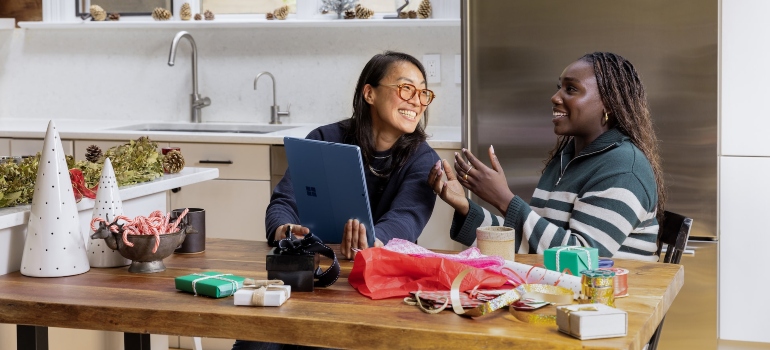 Two women sitting at a kitchen island and looking at a tablet and smiling