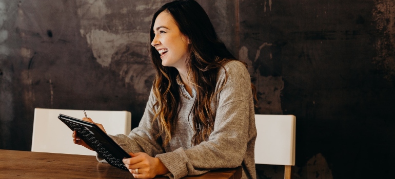 Woman sitting at a table, holding a tablet, and laughing