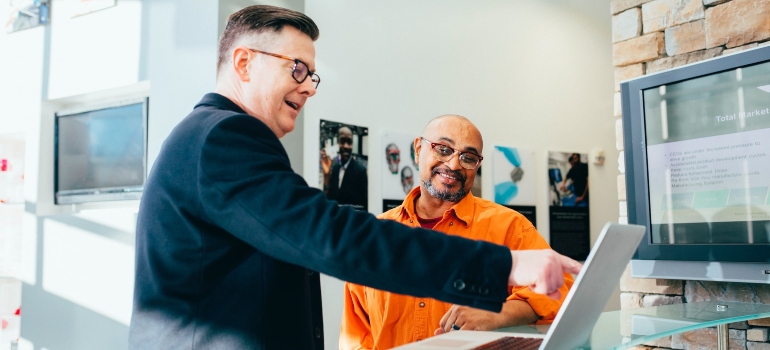 Man smiling and pointing a finger at laptop showing something to another man