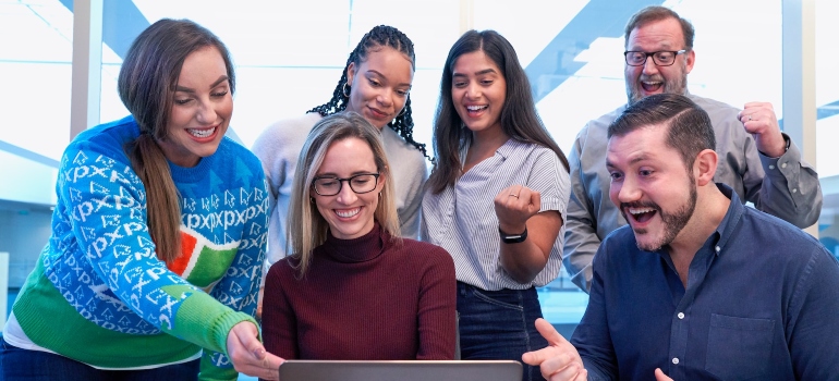 Group of people standing in front of a laptop and smiling