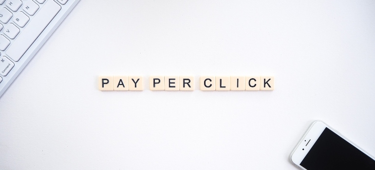 Pay per click written in white blocks with black letters with a keyboard on the left and a smartphone on the right side