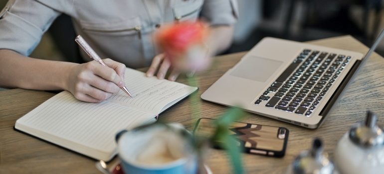 A person writing something in a notebook that's next to a laptop