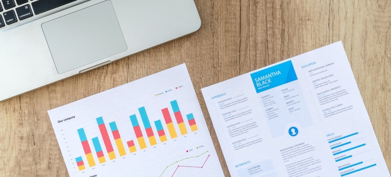 Paper with charts on it next to a MacBook on a wooden desk