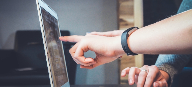 Two people pointing fingers at a laptop screen