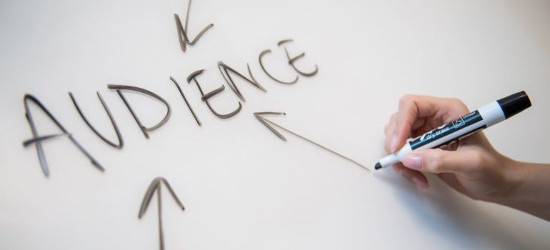 A person writing the word ''audience'' on a whiteboard so as to explain the strategies behind social media for business growth.