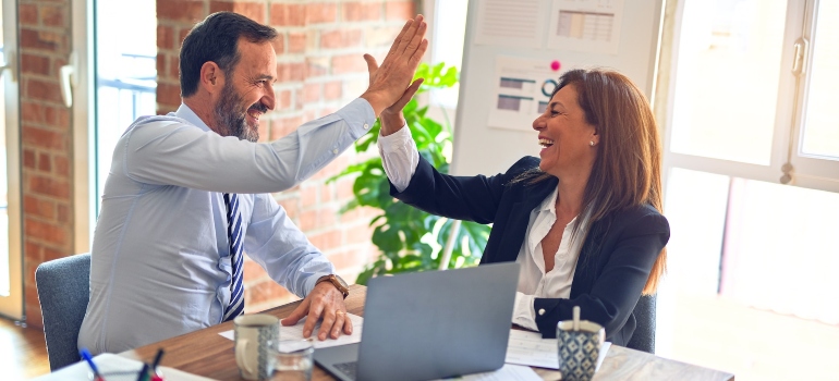 Two people high fiving above a desk to celebrate the launching of their email campaign
