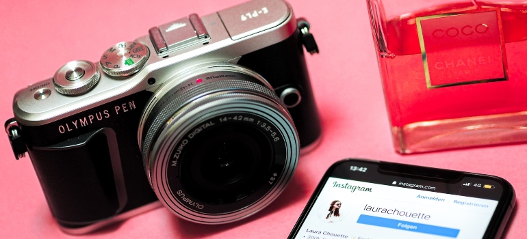 Retro camera and perfume next to a phone with Instagram app opened on it