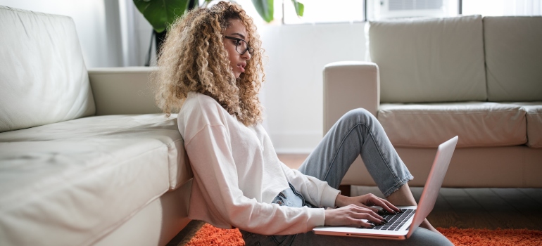 Woman sitting on the floor and researching drug rehab centers on her laptop