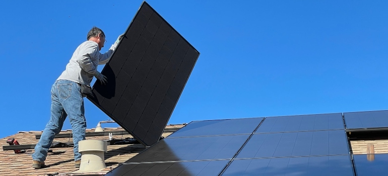 Person installing a solar panel on a roof of a house