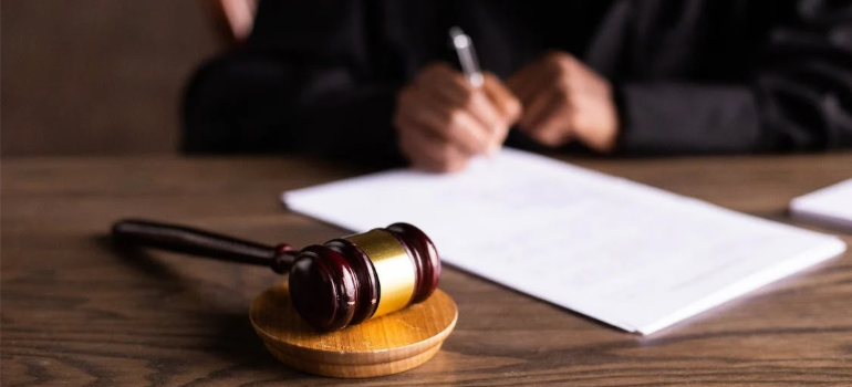 A person writing on a paper next to a gavel, illustrating how the dos and don'ts of alcohol rehab advertising must hinge on regulations.