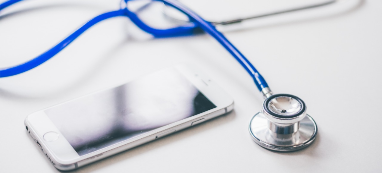 A stethoscope next to a smartphone on a white desk.