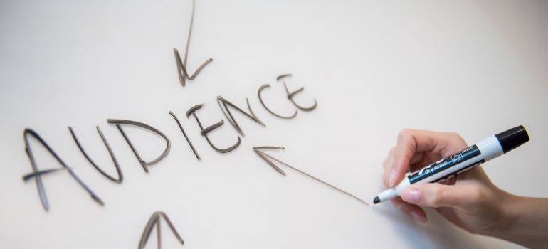 Person using a black marker to draw an arrow pointing at the word audience on a white board