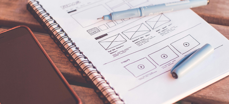 A spiral notebook with website design sketches beside a smartphone, relevant for a workshop on integrating health insurance keywords for rehab clinics into website development.
