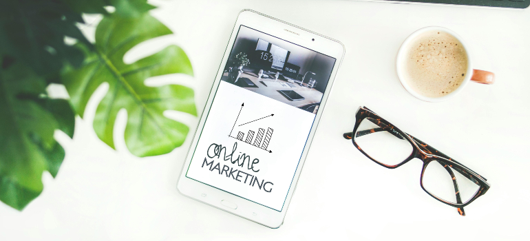A tablet displaying 'online marketing' graph rests on a desk beside a coffee cup and eyeglasses, symbolizing HIPAA compliant digital marketing services.