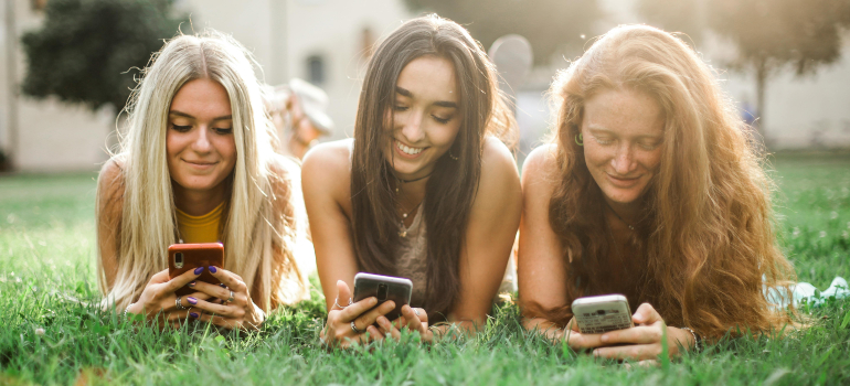 One of the best marketing strategies for telehealth behavioral services is to know your audience, like these three girls laying on the grass holding their phones. 