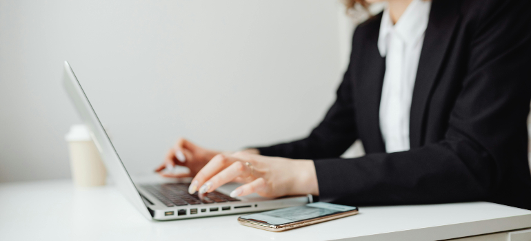 A lawyer in a black suit working on a laptop with a smartphone beside her, highlighting the importance of email marketing strategies for law firms.