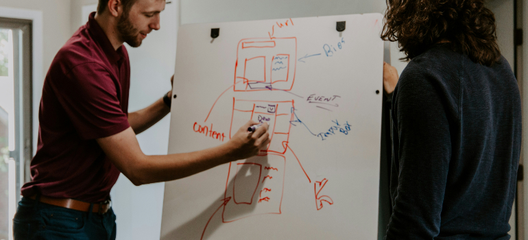 Two people working together on a whiteboard with a web page layout, discussing design and content strategies.