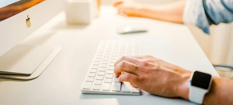 A person typing on a white keyboard in front of a desktop computer, representing focused work on SEO for niche markets.