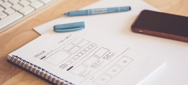 a pen, a phone and a notebook on a wooden desk